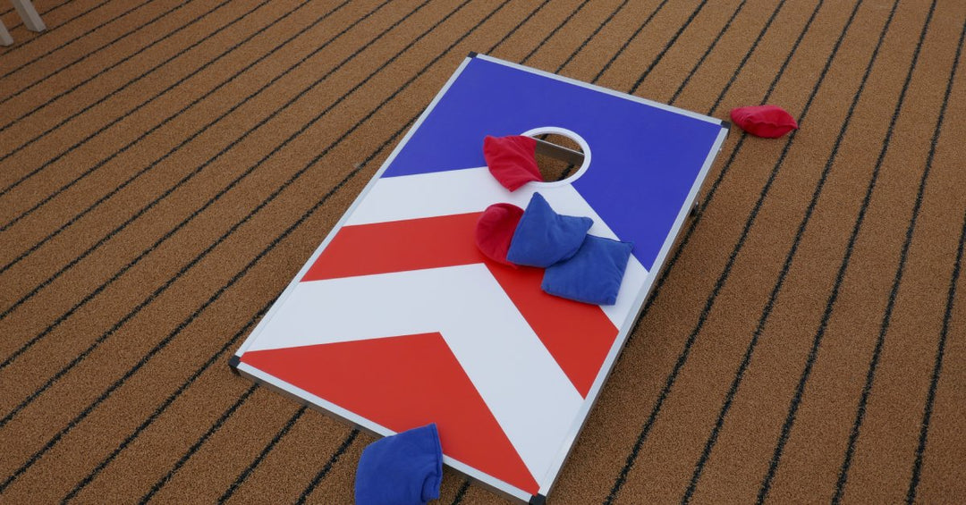 A custom cornhole board with red and white arrows on a blue background. There are red and blue bags on the board.