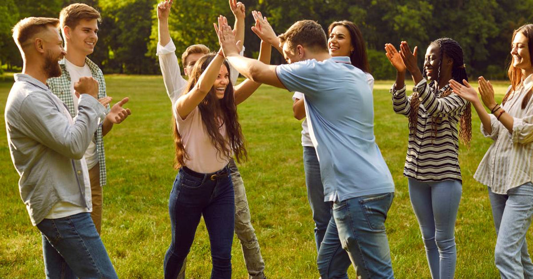 A large group of friends outside in a field of grass. They are celebrating and high-fiving each other.